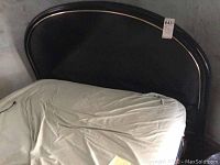 Full view of the bed frame with mattress and wrinkled sheet showing the upholstered black headboard with gold trim.