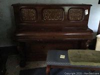 Full view of the upright Cable piano and piano bench side by side, showing carved decorative wood panels and bench cushion.