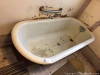 View of the cast iron bathtub showing interior, metal grab bar on the wall, and wooden base it rests on.