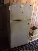 Front view of the white Hotpoint refrigerator showing stains, dirt, and top freezer design.