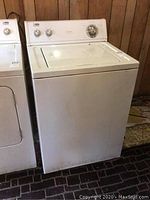 Front and side view of white top-loading Estate washing machine showing overall condition and size relative to adjacent dryer.