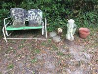 Full view of the vintage glider and surrounding outdoor items arranged on the ground near green foliage.