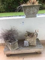 Three cement planters and cherub plaque on wooden platform against low wall