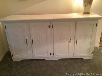Front view of white four door storage cabinet showing carved designs on doors and brass hardware.