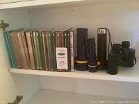 Shelf view showing multiple history-themed DVDs and books plus two flashlights and a pair of field glasses