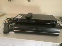 Sony Blu-ray disc player on top of Toshiba VHS DVD player with their remote controls visible on the side and top.