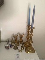 Photo of two brass candle holders with blue candles and various small brass figurines including mice and a bell on a white surface.