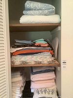 Shelves filled with assorted folded linens including towels, placemats, napkins, and bedding.