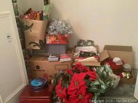 Overall view of Christmas decor and wrapping supplies stacked and boxed together including tins, cards, and artificial greenery.