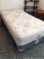 Photo of full single mattress and boxspring on metal bed frame in room with carpet and wooden furniture.