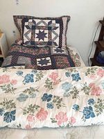 Photo of a bed with a quilt featuring patchwork star design, floral borders, and matching pillow sham in soft colors.