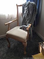 Wooden side chair with beige seat visible, grey throw blanket draped over backrest, chair positioned near window with sunlight.