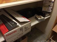 Photo showing Toshiba DVD & VCR combo player box with model SDV398, black electronic device and small boxes on shelves.