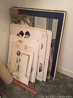 Stack of multiple portrait paintings leaning against wall showing various sizes