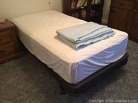 Assembled bed with fitted sheet and folded linens on top.