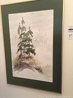 Framed watercolour painting showing a cluster of coniferous trees on a hill with a misty background.