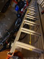 Full view of the aluminum extension ladder showing its length and rungs, lying horizontally in a garage or storage space.