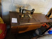 Side view of antique Elgin sewing machine mounted on wooden treadle cabinet with wrought iron base.