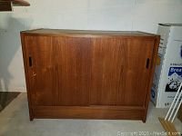 Front view of teak record cabinet with sliding doors closed, showing wood grain and handles.
