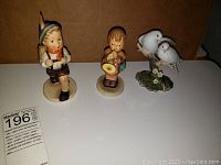 Photo showing the 6-inch Hummel School Boy figurine, the 5-inch Girl with Horn figurine, and a pair of Wings of Love porcelain birds on a base.