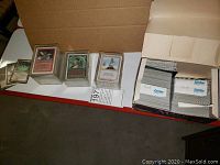 Stacks of sleeved Magic cards in cardboard boxes sorted by color, with a lot identifier visible