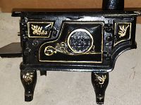 Front view of black PET stovepipe oven miniature with gold decorative accents