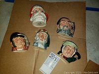 Top-down view of 5 small ceramic Toby mugs arranged on a brown surface, each character mug is distinct with unique features and colors.