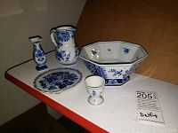 Five-piece set of blue and white Delftware pottery displayed on a table, showing small vase, jug, bowl, plate, and egg cup.