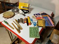Full lot on white table showing two harmonicas, tambourine, microphone, cords, wooden music holders, and band music books