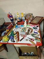 Table top with assorted toys and games, including Simpson figures, promotional pinball and candy dispensers
