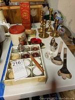 Wide view of lot on table showing Napier silverware, brass candlesticks, vintage tins, and votive candles.