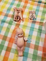 Photo of three ceramic Kewpie dolls laid out on a checkered cloth, showing one large single doll and two smaller doll couples.
