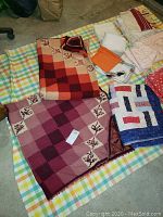 Image showing two handmade blankets with checkered patterns and floral embroidery laid out on a plaid surface alongside vintage linens folded to the side.