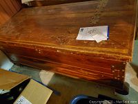 Side view of the cedar chest showing wood grain, wear marks, and metal corner brace.
