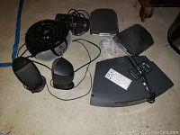 View of Bose Wave Radio remote and several black wired speakers on floor alongside a black round boombox.