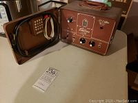 Front and side view of vintage CONN Strobo Tuner Model ST-6 on a table showing the all-metal brown case with carrying handle, control panel with various knobs and tuning meter.