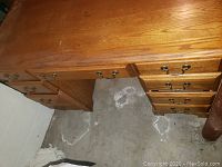 Wooden office desk showing wood grain finish, drawers with brass handles, and surface wear.