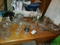 Tabletop display of multiple glass and ceramic items including the Steuben Crystal bowl, Hawkes Crystal pitcher, various smaller candy dishes, vases, and ceramic cookie jar.