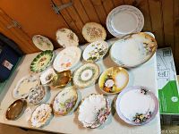 Photo showing assortment of plates and platters in various shapes and designs, laid out on a light-colored table.