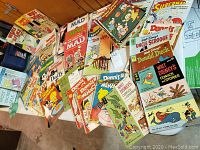Overview of wide selection of vintage comics and magazines from MAD, Dennis the Menace, Disney characters, Superman and more laid out on floor and table.