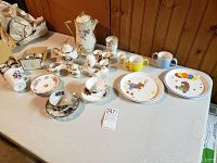 Overview photo showing the entire variety of miscellaneous china items arranged on a table including egg coddlers, children's cups, plates, teapot, and other small dishware