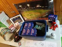 Overall lot on table against wood-paneled wall showing bobblehead boxes in blue case, tin, glove, photos, trading card box, baseball on stand and small framed prints