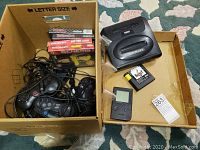 Top-down view showing Sega Genesis console, controllers, boxed games, cables, Game Boy Pocket and loose cartridge