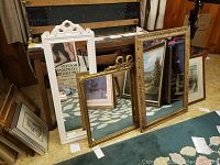 Three mirrors positioned on floor leaning against furniture showing their decorative frames and different sizes.