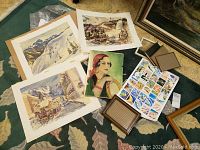 Overall group of art prints, portrait painting, marine grid print and small frames laid out on carpet