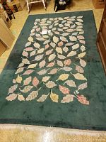 Full view of rectangular green area rug with leaf pattern in muted tones and fringed ends laid out on floor.