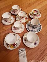 Photo showing 8 assorted porcelain teacups and matching saucers with floral patterns and gold trim.