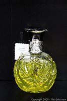 Front view of carved glass perfume bottle with yellow liquid inside, engraved Ralph Lauren logo on center.