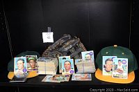 Photo showing the full lot including two baseball caps, stacks of baseball cards, and a black leather left-handed baseball glove.