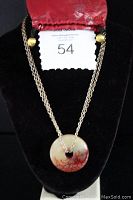 Full view of the necklace displayed on a black bust with the red floral bag on top